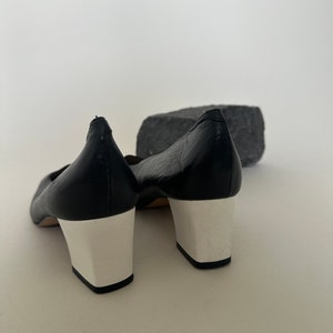 K&ouml;nnte beinhalten: Ein Paar schwarze Lederschuhe mit wei&szlig;en Abs&auml;tzen. Die Schuhe haben eine spitze Zehenpartie und einen niedrigen Absatz.