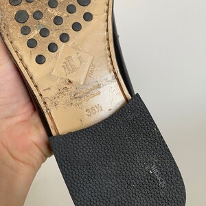 May include: Close-up of the sole of a black leather shoe. The sole is worn, with a rubber heel and a textured rubber sole. The shoe size is 36 1/2. The sole has the words "Vero Cuoio Italy" and the brand "Vibram".