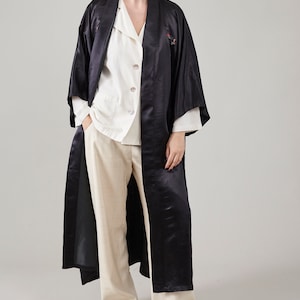 May include: A long black satin robe with a white button-up shirt underneath. The robe has a traditional Japanese style with a wide collar and long sleeves.