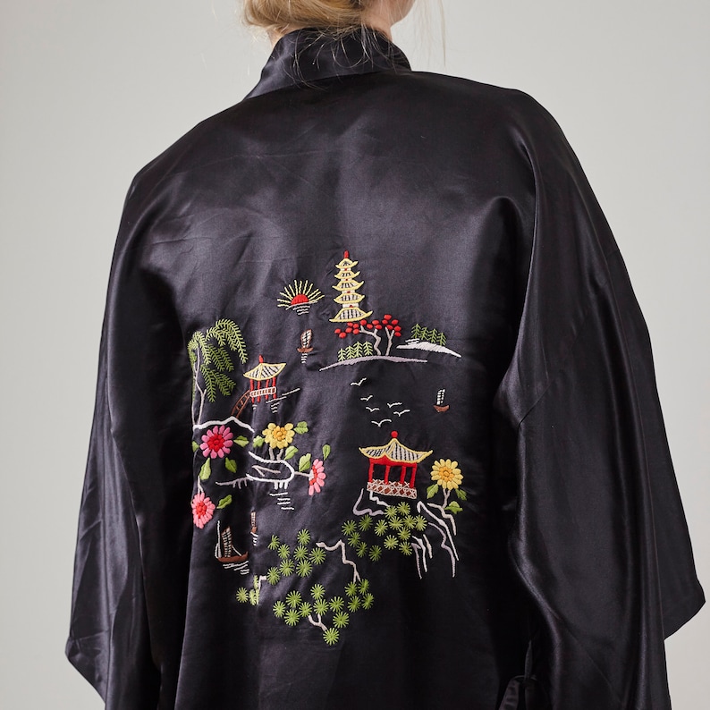 May include: Black satin robe with an embroidered design of a Japanese garden scene. The embroidery features a pagoda, trees, flowers, and birds.