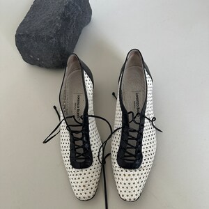 May include: White woven leather shoes with black leather trim and laces. The shoes have a round toe and a low heel. The brand name "Lorenzo Bonfanti" is printed on the inside of the shoes.
