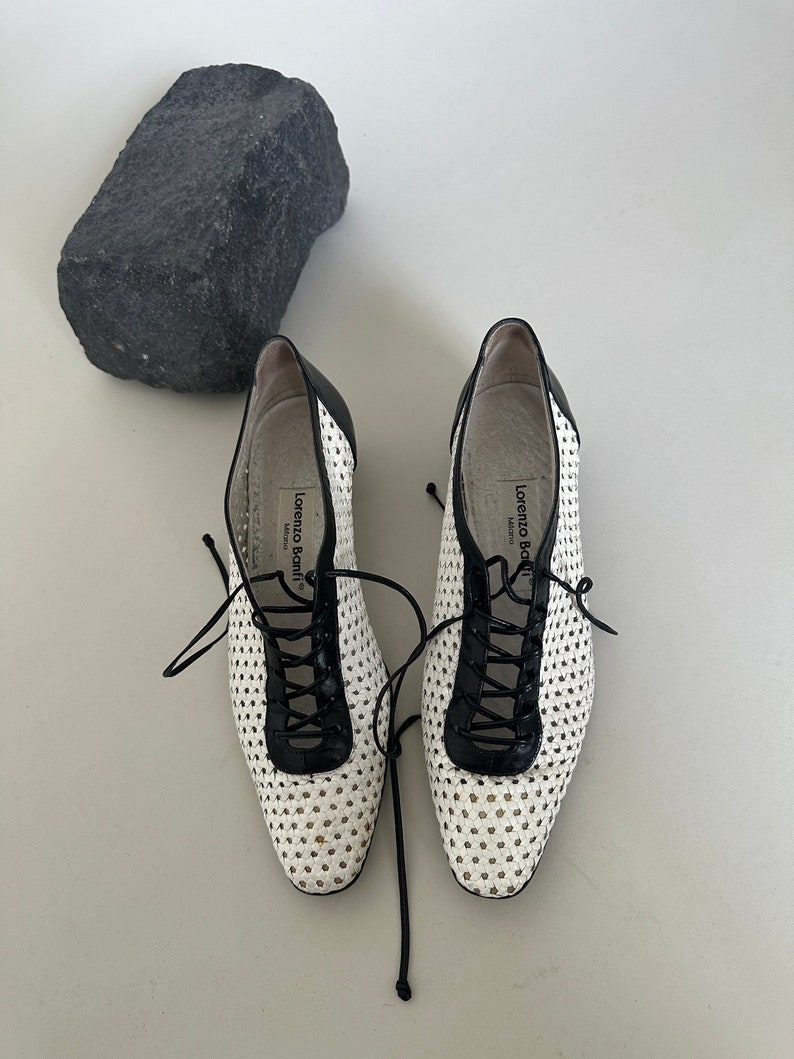 May include: White woven leather shoes with black leather trim and laces. The shoes have a round toe and a low heel. The brand name "Lorenzo Bonfanti" is printed on the inside of the shoes.