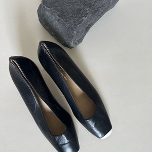 K&ouml;nnte beinhalten: Ein Paar schwarze Lederschuhe mit Absatz, quadratischer Spitze und wei&szlig;em Besatz. Die Schuhe haben eine spitze &Ouml;ffnung an der Oberseite.