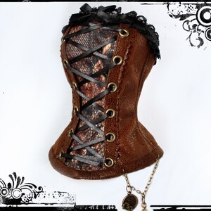 May include: A brown corset with a snakeskin pattern panel, black ribbon lacing, and gold-tone grommets. The corset is trimmed with black lace and a small black bow at the top. A decorative chain with charms hangs from the bottom.