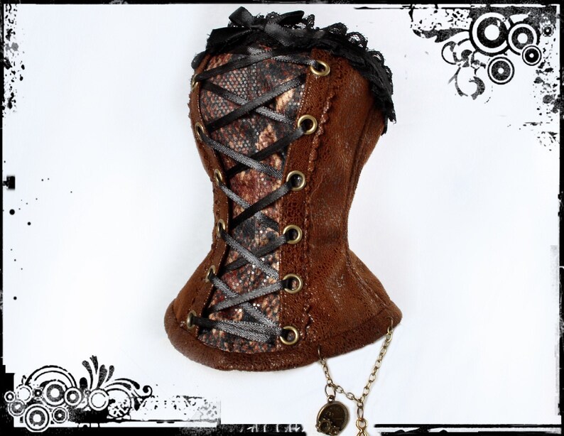 May include: A brown corset with a snakeskin pattern panel, black ribbon lacing, and gold-tone grommets. The corset is trimmed with black lace and a small black bow at the top. A decorative chain with charms hangs from the bottom.
