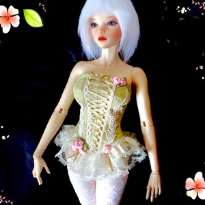 May include: A doll with white hair and blue eyes, wearing a green corset with lace detailing and pink rose accents. The doll's outfit includes a white lace skirt and white patterned leggings. The background is black with floral decorations.