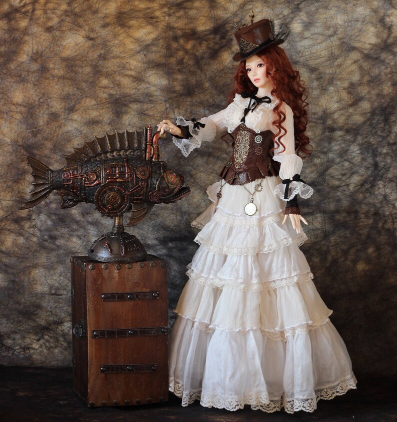Op de afbeelding: Een steampunk-pop met rood haar, een bruine hoge hoed, een witte ruchesjurk en een bruin korset. Naast de pop staat een gedetailleerde, mechanische vissculptuur op een houten kist, die Victoriaanse en industri&euml;le elementen combineert.