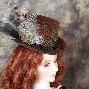 Op de afbeelding: Een bruine steampunk-stijl hoge hoed met een getextureerde afwerking. De hoed is versierd met veren, zwart gaas en decoratieve tandwielen. Een gouden filigraanontwerp accentueert de voorkant. Een uniek accessoire voor cosplay.