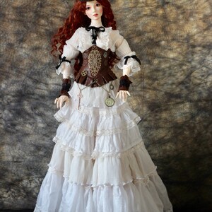 Op de afbeelding: Een pop gekleed in een steampunk-ge&iuml;nspireerde outfit. De pop heeft lang rood haar en draagt een bruine hoge hoed, een witte blouse met kanten rand en een bruin korset. De rok is wit met meerdere gefranjerde lagen. Accessoires zijn een sleutelhanger en een zakhorloge.