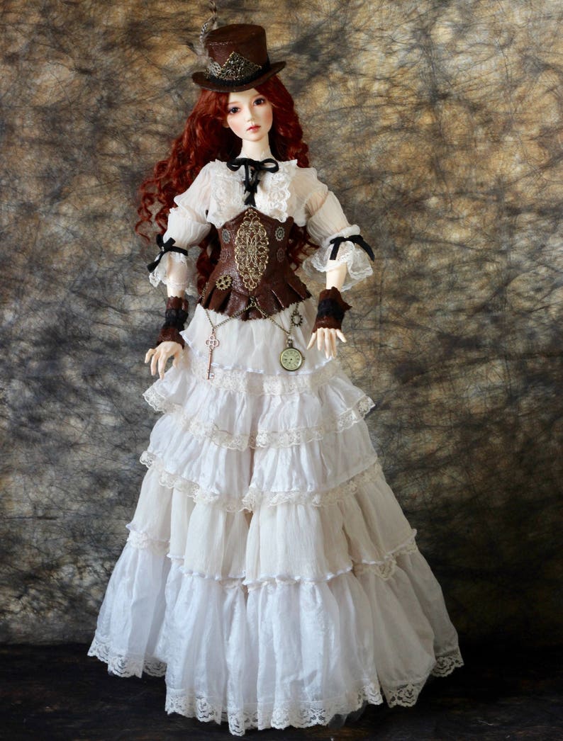 Op de afbeelding: Een pop gekleed in een steampunk-ge&iuml;nspireerde outfit. De pop heeft lang rood haar en draagt een bruine hoge hoed, een witte blouse met kanten rand en een bruin korset. De rok is wit met meerdere gefranjerde lagen. Accessoires zijn een sleutelhanger en een zakhorloge.
