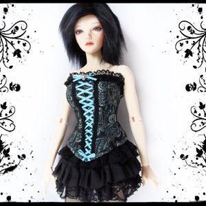 May include: A doll wearing a black and teal corset with a floral pattern, laced with light blue ribbon. The corset is paired with a black ruffled skirt and lace trim. The doll has black hair and is set against a white background.