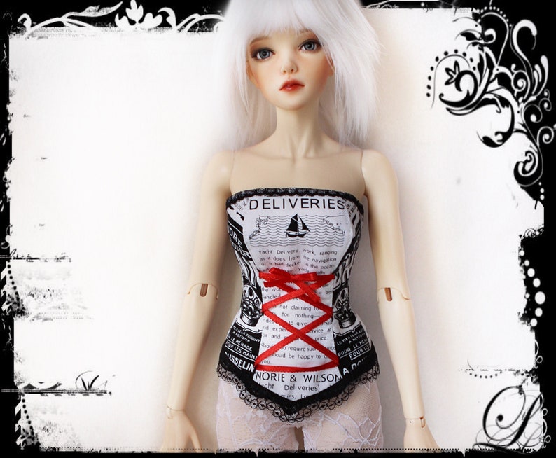 May include: A white and black corset with a red ribbon, featuring text and a sailboat illustration. The corset has a black lace trim and is worn by a doll with white hair.