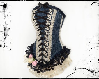 May include: A denim corset with black ribbon lacing and a black bow at the top. The corset is trimmed with cream-colored lace and black lace along the bottom, with small pink and white roses.