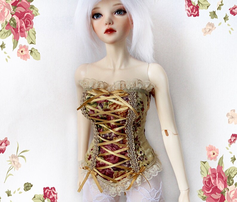 May include: A doll wearing a floral corset with gold ribbon lacing. The corset features a mix of burgundy, green, and gold floral patterns. The doll has white hair and is wearing white lace stockings. The background has a floral design.