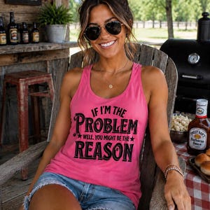 Könnte beinhalten: Ein leuchtend pinkfarbenes ärmelloses Tanktop mit dem schwarzen Aufdruck IF I'M THE PROBLEM WELL, YOU MIGHT BE THE REASON und Sternenmotiven. Das Kleidungsstück hat einen Rundhalsausschnitt und einen Ringerrücken, kombiniert mit hellblauen Jeansshorts.