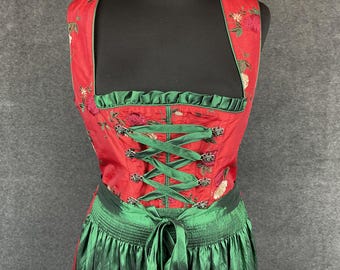 Puede incluir: Un dirndl rojo y verde con un corpiño bordado con flores y una falda verde. El corpiño tiene un cordón de cinta verde que se ata en la parte delantera.