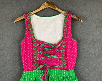 Puede incluir: Un vestido tradicional alemán, llamado dirndl, con un corpiño blanco y una falda verde y blanca. El corpiño está adornado con bordes verdes y un cordón en la parte delantera con cintas rosas.