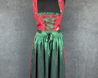 Puede incluir: Un vestido tradicional alemán, llamado dirndl, rojo y verde con estampado floral y ribete de encaje. El corpiño tiene un cierre de encaje en la parte delantera y la falda es amplia y plisada.