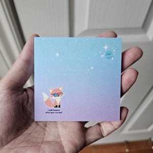 Op de afbeelding: Een blauwe en paarse verloopkleefbriefje met een cartoonvos die een bril draagt en de tekst "Kijk verder dan wat je kunt zien!" Een kleine blauwe planeet met een glimlachend gezicht bevindt zich in de rechterbovenhoek.