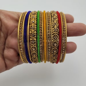 Puede incluir: Un conjunto de pulseras doradas con intrincados dise&ntilde;os florales y gemas incrustadas. El conjunto incluye pulseras en varios colores, como azul, verde, amarillo y rojo, creando un aspecto vibrante y ornamentado. Las pulseras se sostienen en una mano.