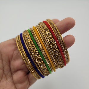 Puede incluir: Un conjunto de pulseras doradas con intrincados dise&ntilde;os florales y pedrer&iacute;a incrustada. Las pulseras presentan una variedad de colores, incluyendo rojo, amarillo, verde y azul, creando un accesorio vibrante y llamativo.