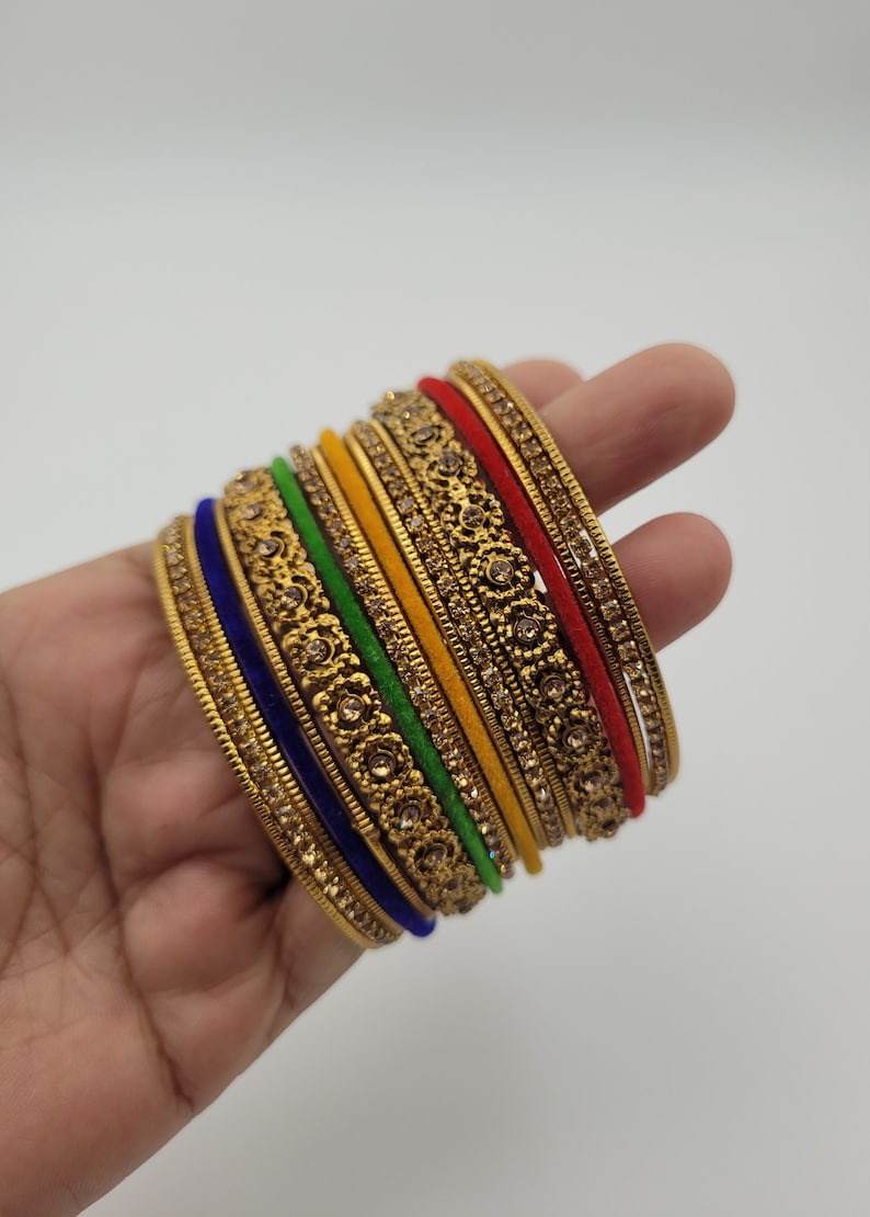 Puede incluir: Un conjunto de pulseras doradas con intrincados dise&ntilde;os florales y pedrer&iacute;a incrustada. Las pulseras presentan una variedad de colores, incluyendo rojo, amarillo, verde y azul, creando un accesorio vibrante y llamativo.