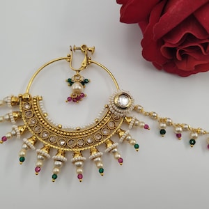May include: Gold-toned nose ring with intricate detailing, featuring clear stones, pearls, and colorful accents. The design includes a large hoop, a clip, and a chain with dangling beads. A red rose is in the background.