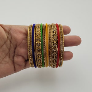 Puede incluir: Un conjunto de pulseras doradas con intrincados dise&ntilde;os florales y pedrer&iacute;a incrustada. El conjunto incluye pulseras en varios colores, como azul, verde, amarillo y rojo, creando un accesorio vibrante y llamativo.