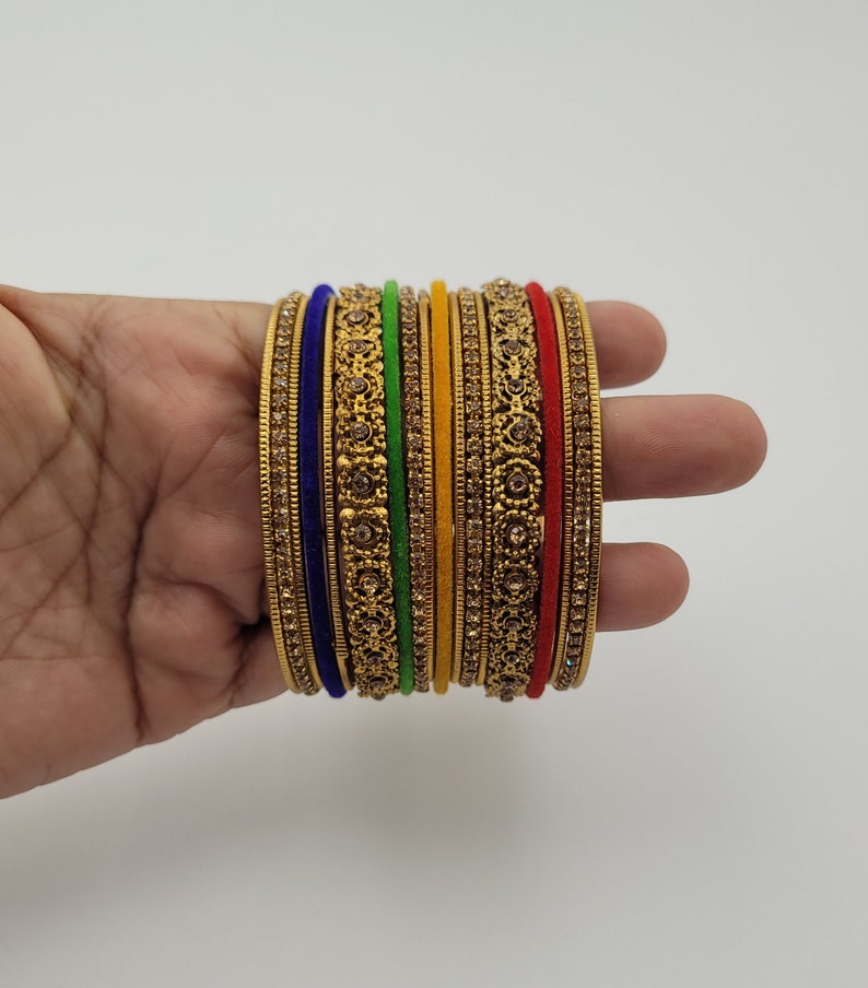 Puede incluir: Un conjunto de pulseras doradas con intrincados dise&ntilde;os florales y pedrer&iacute;a incrustada. El conjunto incluye pulseras en varios colores, como azul, verde, amarillo y rojo, creando un accesorio vibrante y llamativo.