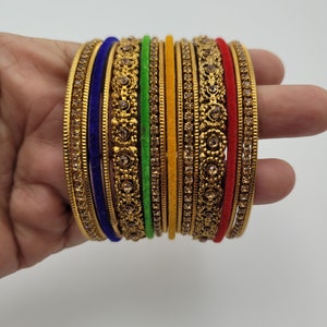 Puede incluir: Un conjunto de pulseras doradas con intrincados dise&ntilde;os florales y gemas incrustadas. El conjunto incluye pulseras en varios colores, como azul, verde, amarillo y rojo, creando un accesorio vibrante y llamativo.