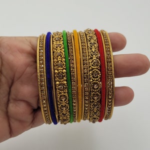 Puede incluir: Un conjunto de pulseras doradas con intrincados dise&ntilde;os florales y pedrer&iacute;a incrustada. El conjunto incluye pulseras en varios colores, como azul, verde, amarillo y rojo, creando un accesorio vibrante y llamativo.
