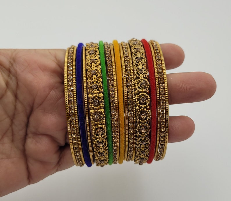 Puede incluir: Un conjunto de pulseras doradas con intrincados dise&ntilde;os florales y pedrer&iacute;a incrustada. El conjunto incluye pulseras en varios colores, como azul, verde, amarillo y rojo, creando un accesorio vibrante y llamativo.