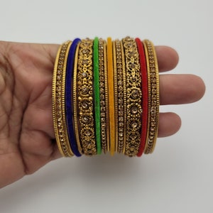 Puede incluir: Un conjunto de pulseras doradas con intrincados dise&ntilde;os florales y pedrer&iacute;a incrustada. El conjunto incluye pulseras en varios colores, como azul, verde, amarillo y rojo, creando un accesorio vibrante y llamativo.