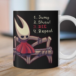Pode incluir: Caneca de cerâmica preta com um personagem de desenho animado em um vestido vermelho e máscara branca, sentado em um banco de madeira. A caneca tem o texto "1. Jump 2. Shaw! 3. DIE 4. Repeat" em branco.