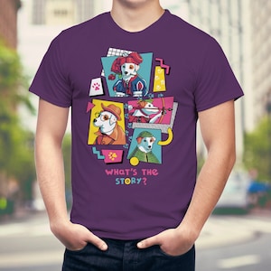 Op de afbeelding: Een paars T-shirt met een kleurrijk grafisch ontwerp van vier honden in verschillende kostuums. Het ontwerp bevat de tekst "WHAT'S THE STORY?" in roze en geel. De honden zijn gekleed in verschillende outfits, waaronder een koninklijk kostuum, een detective-outfit en een jagersoutfit.