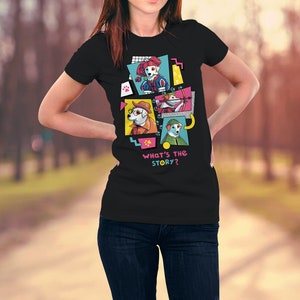 Op de afbeelding: Zwart t-shirt met een kleurrijke afbeelding van cartoonhonden in verschillende outfits. Het ontwerp bevat de tekst "WHAT'S THE STORY?" in roze en blauw. De honden zijn afgebeeld in een pop-art stijl, met felle kleuren en geometrische vormen.