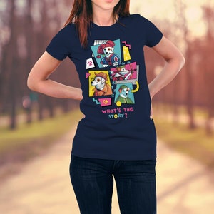 Op de afbeelding: Marineblauw T-shirt met een kleurrijke afbeelding van cartoonhonden in verschillende outfits. Het ontwerp bevat de tekst "WHAT'S THE STORY?" in een speels lettertype. Het shirt is een klassieke ronde hals.