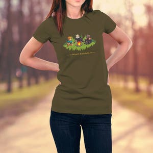 May include: A woman wearing a green t-shirt with a cartoon image of three characters around a campfire. The text "World's Explorers" is printed below the image.