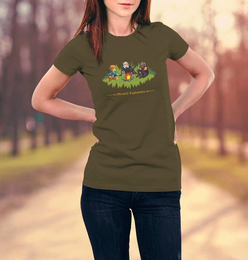 May include: A woman wearing a green t-shirt with a cartoon image of three characters around a campfire. The text "World's Explorers" is printed below the image.