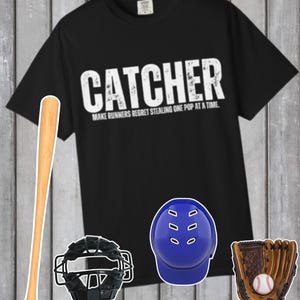 Op de afbeelding: Zwart T-shirt met het woord "CATCHER" in witte blokletters. Het shirt heeft ook de tekst "MAKE RUNNERS REGRET STEALING ONE POP AT A TIME." Honkbalknuppel, catcher's mask, blauwe helm en honkbalhandschoen met een bal.