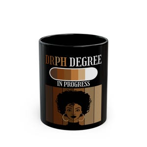 May include: Black ceramic mug with the text "DRPH DEGREE IN PROGRESS" in gold lettering. The mug features a graphic of a woman with large hoop earrings and a gradient of skin tones. The mug is a standard 11 oz size.