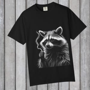 May include: Black t-shirt featuring a detailed black and white illustration of a raccoon holding a cigarette. The raccoon is depicted with a serious expression, and smoke curls upwards from the cigarette. The t-shirt is made of a soft material.