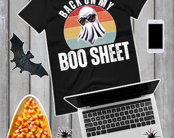 以下が含まれることがあります： 「BACK ON MY BOO SHEET」の文字とサングラスをかけたお化けのグラフィックがプリントされた黒いTシャツ。画像には、ラップトップ、スマートフォン、キャンディーコーン、クモ、コウモリ、メガネも含まれています。