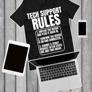May include: Black t-shirt with the text "TECH SUPPORT RULES" and instructions. The image includes a laptop, tablet, smartphone, and eyeglasses, all on a wooden surface.