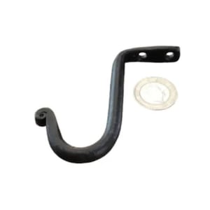 May include: A black, wrought iron hook with a curved design. The hook has a decorative curled end and a flat mounting plate with two holes. A small, round object is next to the hook.
