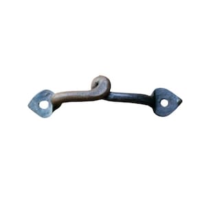 May include: A wrought iron hook and eye latch with a rustic appearance. The latch has a curved hook and heart-shaped end pieces. The metal has a dark, aged finish, suggesting an antique or vintage style. Suitable for doors or gates.