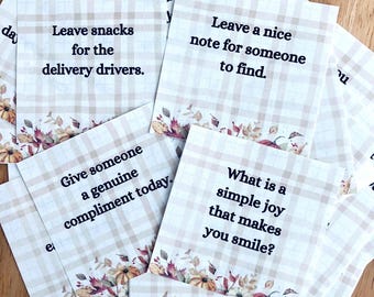 May include: A collection of square cards with fall-themed illustrations and text. The cards have a beige and white plaid pattern and feature phrases like "Leave snacks for the delivery drivers" and "Give someone a genuine compliment today."