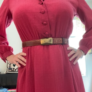 May include: A long-sleeved, red dress with a button-up front and a brown leather belt with a gold buckle.