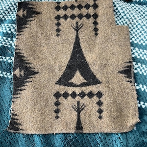 May include: A rectangular piece of tan felted fabric featuring a black printed pattern. The design includes a central black teepee motif flanked by geometric diamond shapes and vertical lines, with a jagged black border along the left side.