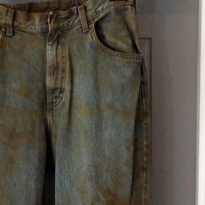 Puede incluir: Un par de pantalones vaqueros azules con manchas marrones y dobladillos deshilachados.